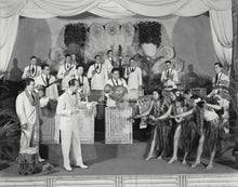Load image into Gallery viewer, Black and white photo of bandleader Harry Owens leading the Royal Hawaiian Orchestra and accompanied by female hula dancers.