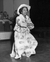Load image into Gallery viewer, Black and white photograph of Hilo Hattie dancing the hula wearing a long mumu and hat.