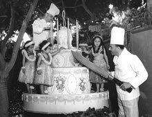 Load image into Gallery viewer, Black and white photo of a large cake surrounded by chefs, one holding an oversized knife, and girls in hula dresses.