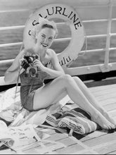 Load image into Gallery viewer, Black and white photograph of a woman in the 1950’s holding a camera wearing a bathing suit and sitting on the deck of a cruise ship with a life preserver hanging on the rail behind her. “S.S.Lurline Honolulu” written on the life preserver.